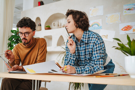 Graphic designer discussing with colleague leaning on desk at office