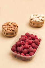 Raspberries and walnuts in plastic containers. Nuts in wooden boxes.  Plastic pollution and eco-friendly dish
