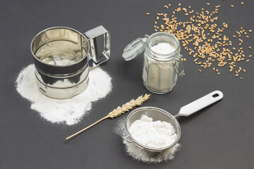 Mug for sifting flour and small sieve with flour, glass jar with flour. Wheat spikelet and wooden spoon.