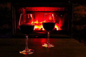 Two glasses of red wine on a background of a burning fireplace. Cozy atmosphere winter evening.