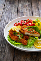 Crispy breaded fried chicken cutlet with fresh vegetables and boiled potatoes on wooden table

