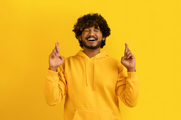 Superstitious indian guy with closed eyes and crossed fingers - obrazy, fototapety, plakaty
