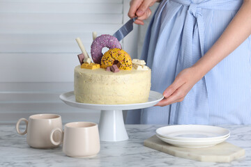 Woman cutting delicious cake decorated with sweets at white marble table, closeup
