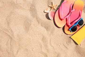 Fototapeta na wymiar Flip flops and other beach accessories on sand, flat lay. Space for text