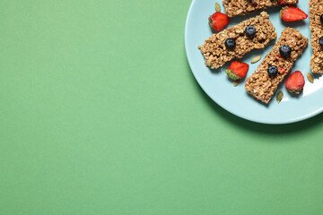 Tasty granola bars and berries on green background, top view. Space for text