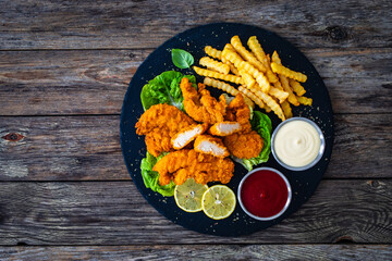 Fried breaded chicken nuggets served with French fries and vegetables on wooden table
