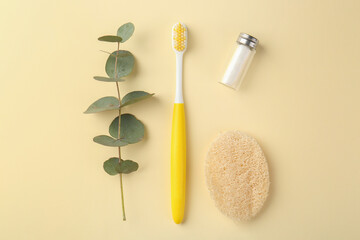 Plastic toothbrush, eucalyptus branch and other toiletries on pale yellow background, flat lay