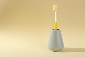 Plastic toothbrush in holder on pale yellow background, space for text