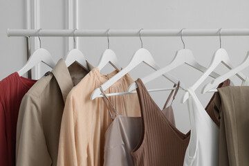 Rack with different stylish women`s clothes near white wall indoors, closeup