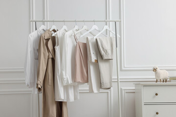 Rack with different stylish women`s clothes and dresser near white wall in room