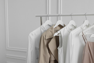 Rack with different stylish women`s clothes near white wall indoors, space for text