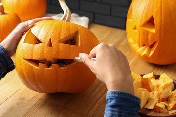 Woman carving pumpkin at wooden table, closeup. Halloween celebration