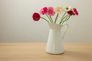 Jug with beautiful gerbera flowers on wooden table. Space for text
