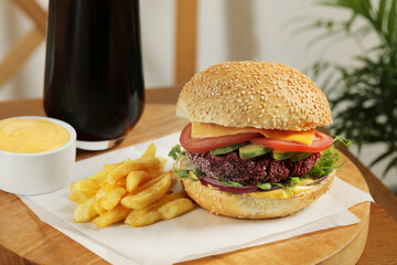 Tasty vegetarian burger served with french fries and sauce on wooden table, closeup