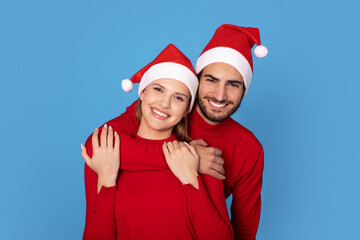 Cheerful Couple Wearing Red Sweaters And Santa Hats Posing On Blue Background