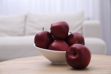 Bowl with red apples on wooden table in room, closeup