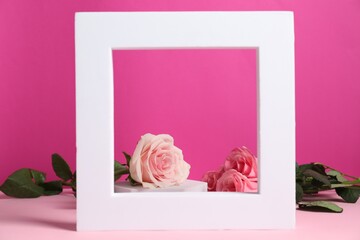 Stylish presentation of product. Beautiful roses behind white frame on pink table
