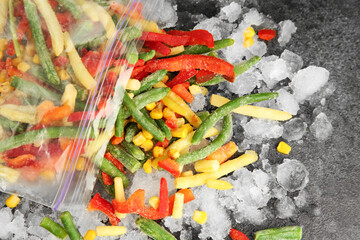 Zip bag with different frozen vegetables and ice on grey table, top view