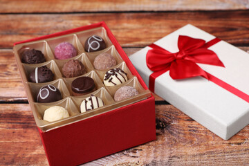 Red box with tasty chocolate candies on wooden table, closeup