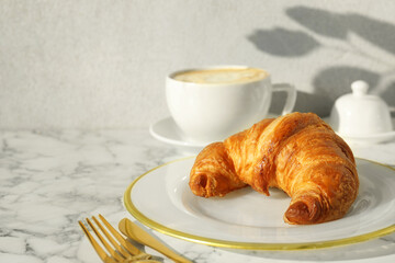 Delicious fresh croissant served with coffee on white marble table, closeup. Space for text