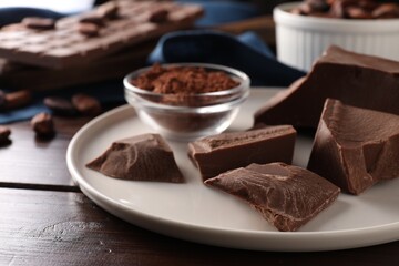 Pieces of tasty milk chocolate and powder on wooden table, closeup