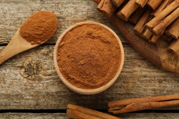 Bowl of cinnamon powder and sticks on wooden table, flat lay