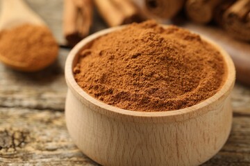 Bowl of cinnamon powder on wooden table, closeup