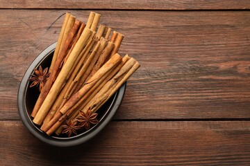 Bowl with cinnamon sticks and star anise on wooden table, top view. Space for text