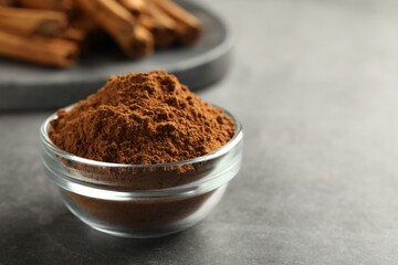 Bowl of cinnamon powder on grey table, closeup. Space for text