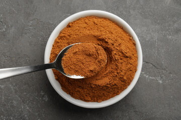 Taking cinnamon powder with spoon from bowl on grey table, top view