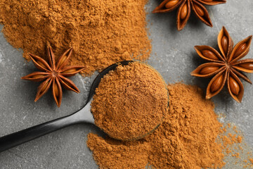Spoon with cinnamon powder and star anise on grey table, flat lay