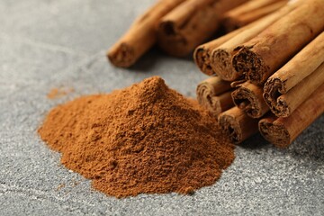 Cinnamon powder and sticks on grey table, closeup