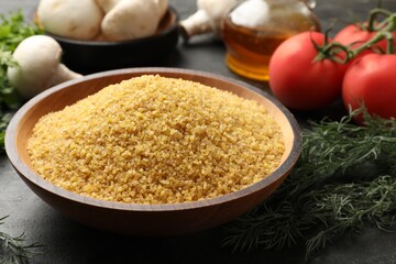 Raw bulgur in bowl, dill and vegetables on table, closeup