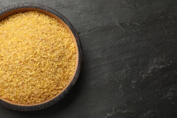 Raw bulgur in bowl on dark gray table, top view. Space for text