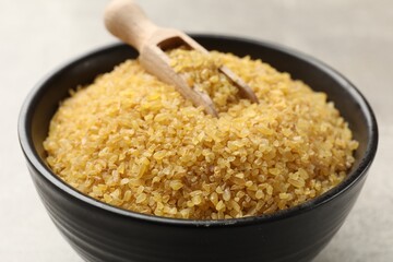 Bowl and scoop with raw bulgur on gray background, closeup