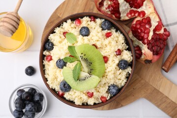 Bowl of tasty couscous with kiwi, blueberries, pomegranate and honey on white table, flat lay