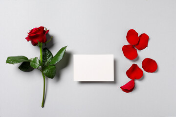 Blank card, beautiful red rose and petals on light background, flat lay. Space for text