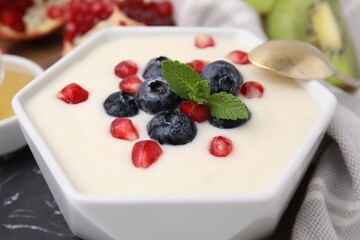 Bowl of delicious semolina pudding with blueberries, pomegranate and mint served on table, closeup
