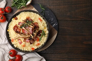 Bowl of tasty couscous with mushrooms, bacon and tomatoes on wooden table, flat lay. Space for text