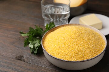 Raw cornmeal in bowl, butter and parsley on wooden table, closeup. Space for text