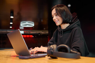 European brunette woman in hoodie sitting with laptop in cafe