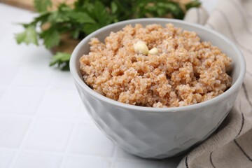 Tasty wheat porridge with butter in bowl on white tiled table, closeup. Space for text
