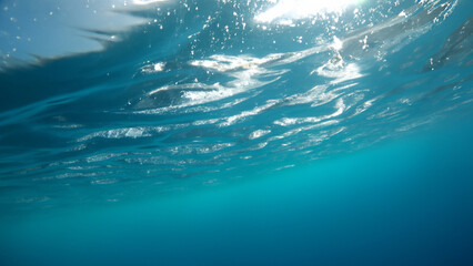 Underwater view of the sea surface with ripples and sunlight, clear blue water, copy space