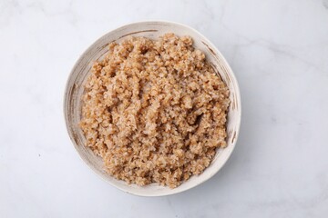 Tasty wheat porridge in bowl on white marble table, top view