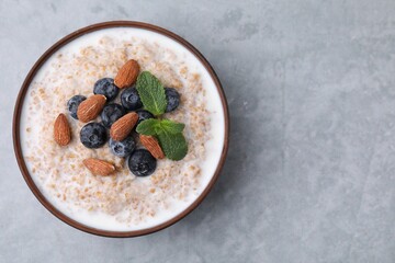Tasty wheat porridge with milk, blueberries and almonds in bowl on gray table, top view. Space for text - obrazy, fototapety, plakaty