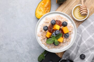 Tasty wheat porridge with pumpkin, dates and blueberries in bowl on light gray table, flat lay. Space for text