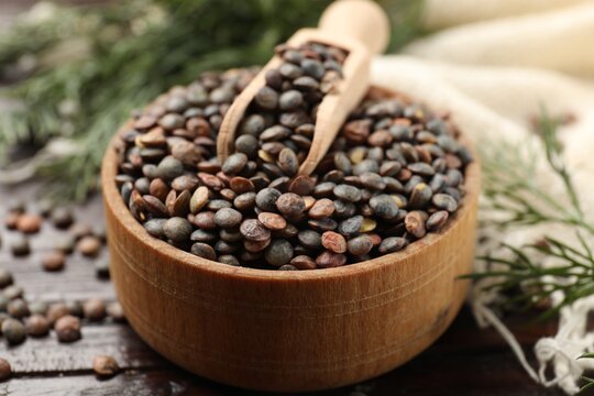 Raw lentils and scoop in bowl on wooden table, closeup