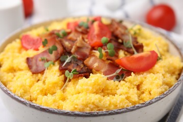 Tasty cornmeal with tomatoes, bacon and microgreens in bowl, closeup