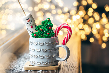 Hot drink with marshmallows, gingerbread and candy cane in mug.