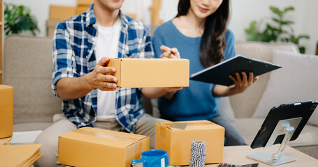 Startup small business SME, Entrepreneur owner man and woman using smartphone or tablet taking receive and checking online purchase shopping order to preparing pack product box. on sofa .